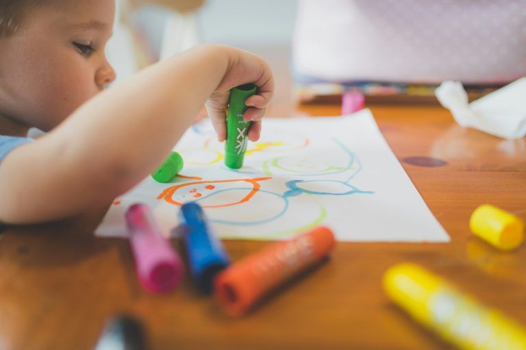 Close-up of a child's hand holding a green marker and drawing on a piece of paper