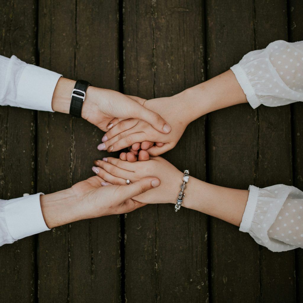 Close-up of two people's hands clasped together on a wooden surface, symbolizing support and connection